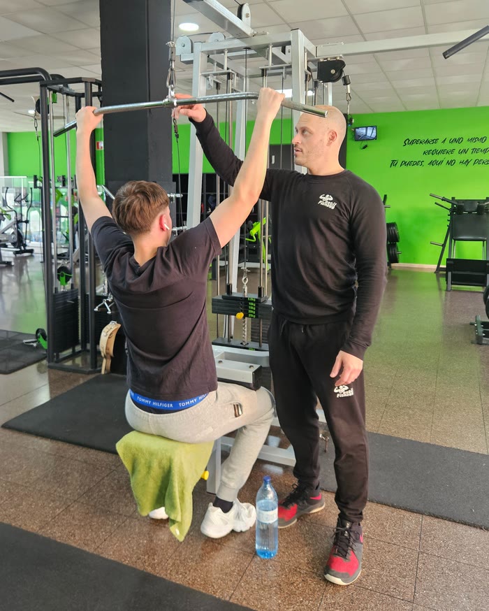 Un instructor de EstilFitness corrige la técnica de un socio en el jalón